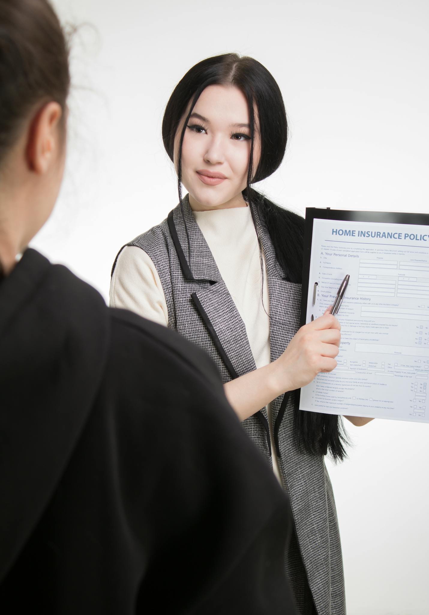 Young Asian businesswoman explaining home insurance policy to client, highlighting details with pen.